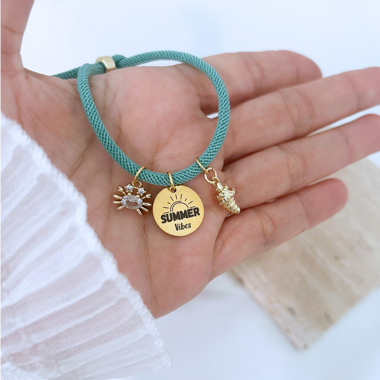 Hand holding a teal cord bracelet with polished gold hardware and summer-inspired charms. The lightweight adjustable design combines coastal style with elegant gold details, perfect for everyday wear or vacations.