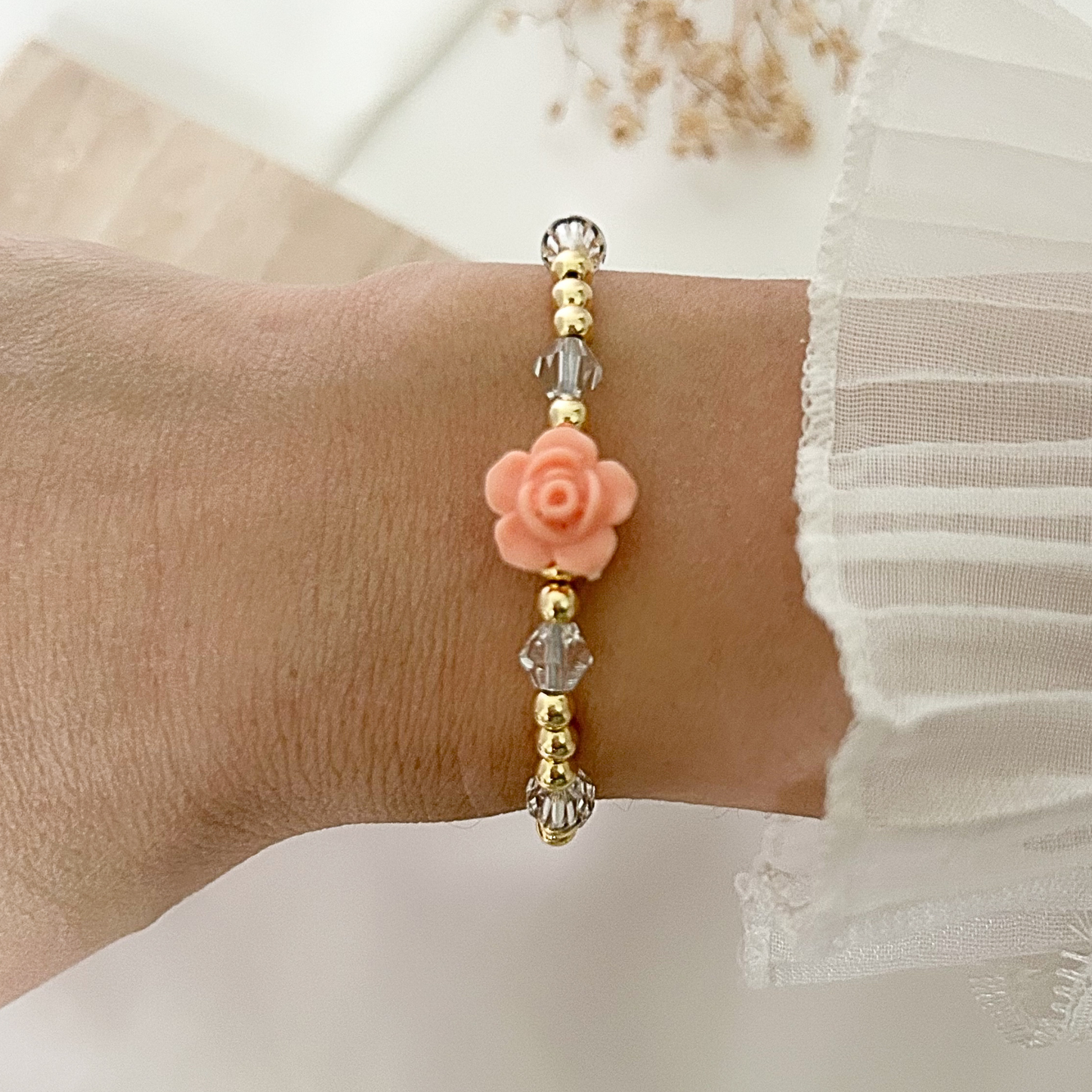 Elegant bracelet with a soft peach resin rose, gold-tone beads, and crystal accents, worn on the wrist for a delicate and romantic style.