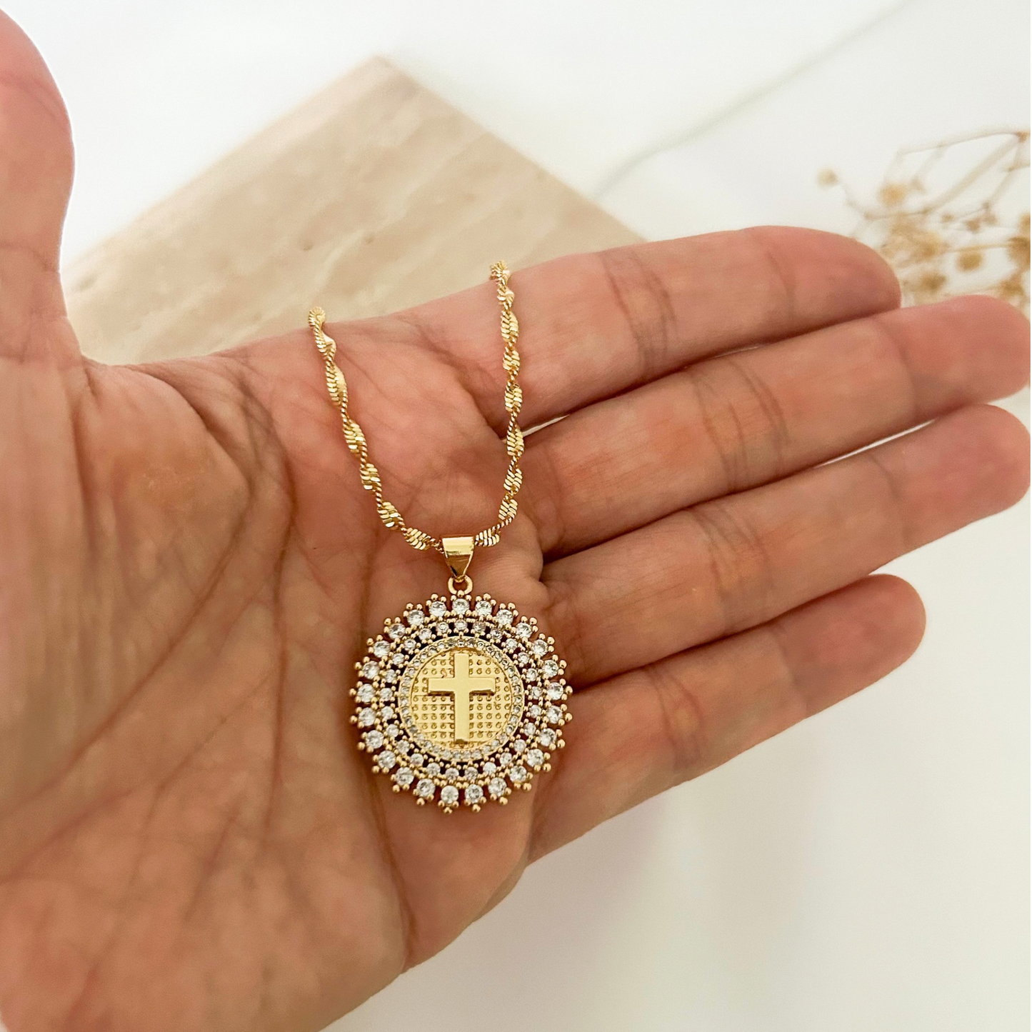 Close-up of an elegant gold necklace with a sparkling circular cross pendant surrounded by brilliant crystal accents and a textured twisted chain for added sophistication.
