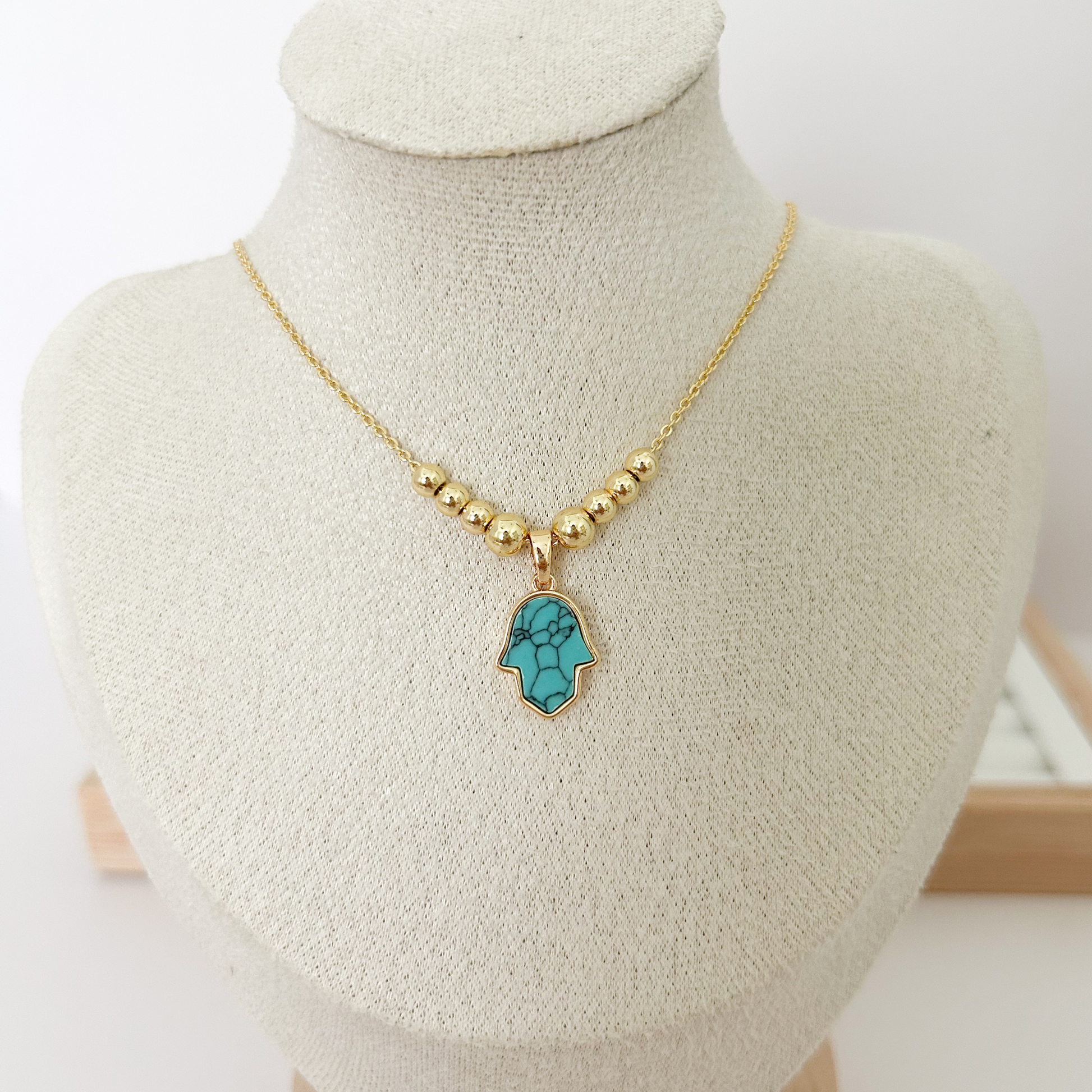 Gold beaded necklace with turquoise Hamsa hand pendant on linen jewelry bust — Citrika