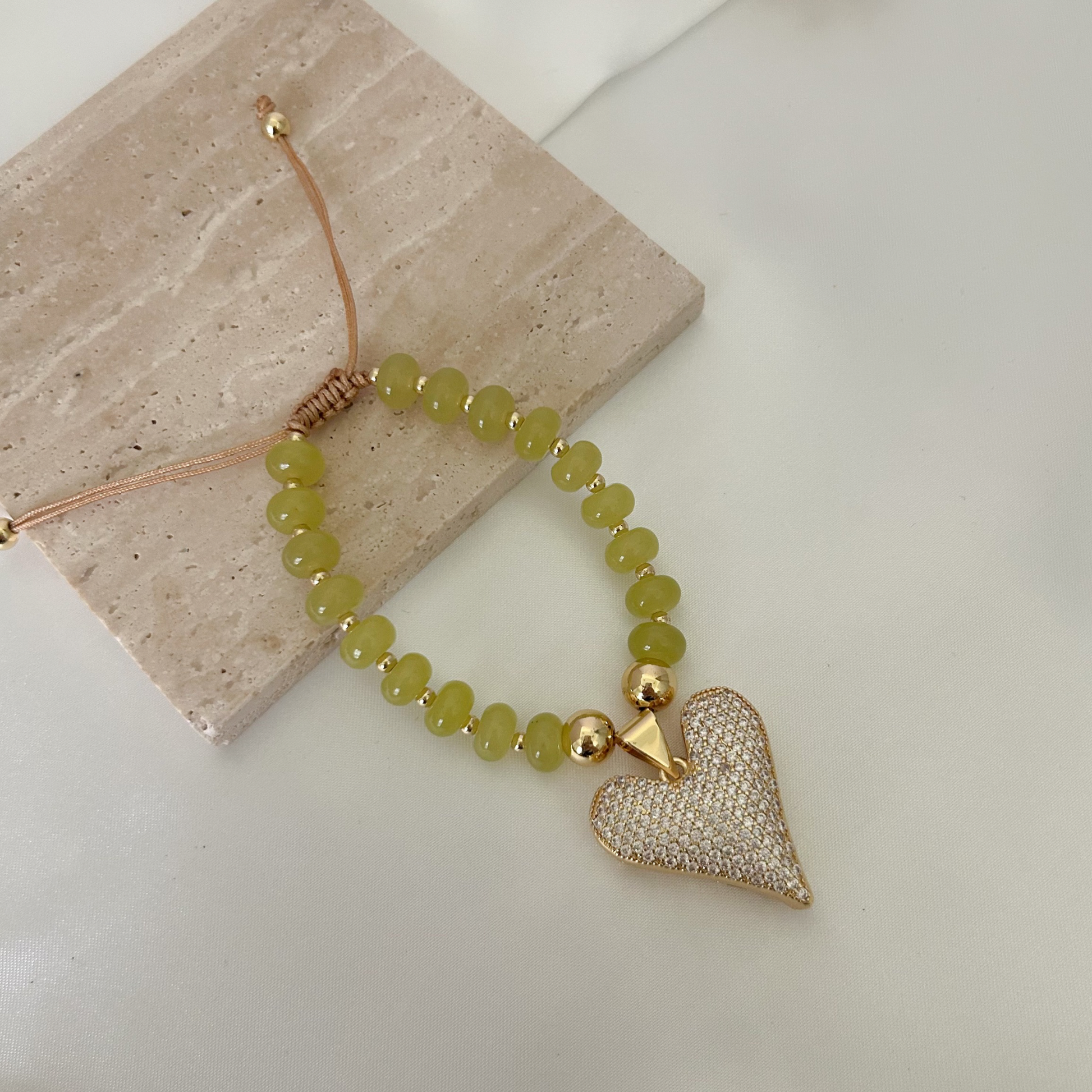 Close-up of a statement heart bracelet with faceted crystal details, gold-tone beads, and an adjustable cord closure.