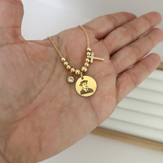 Gold necklace with a pendant featuring a portrait held in a hand against a white background