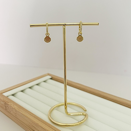 Gold huggie hoop earrings with dangling seashell charm on jewelry stand