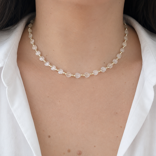 Elegant heart-shaped bead necklace worn on a model, combining soft translucent beads with gold-tone details for a romantic everyday look.
