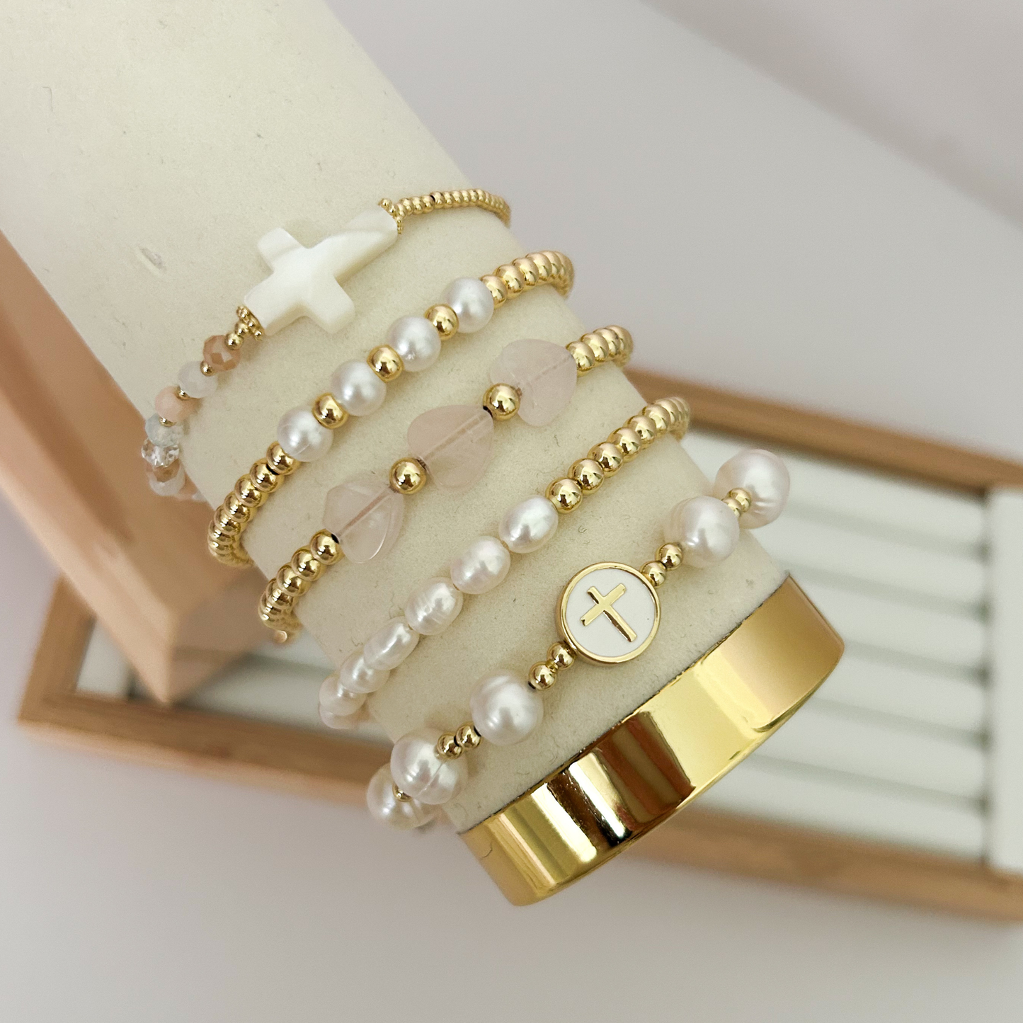 Pink pearl cross gold bracelet set displayed on jewelry stand
