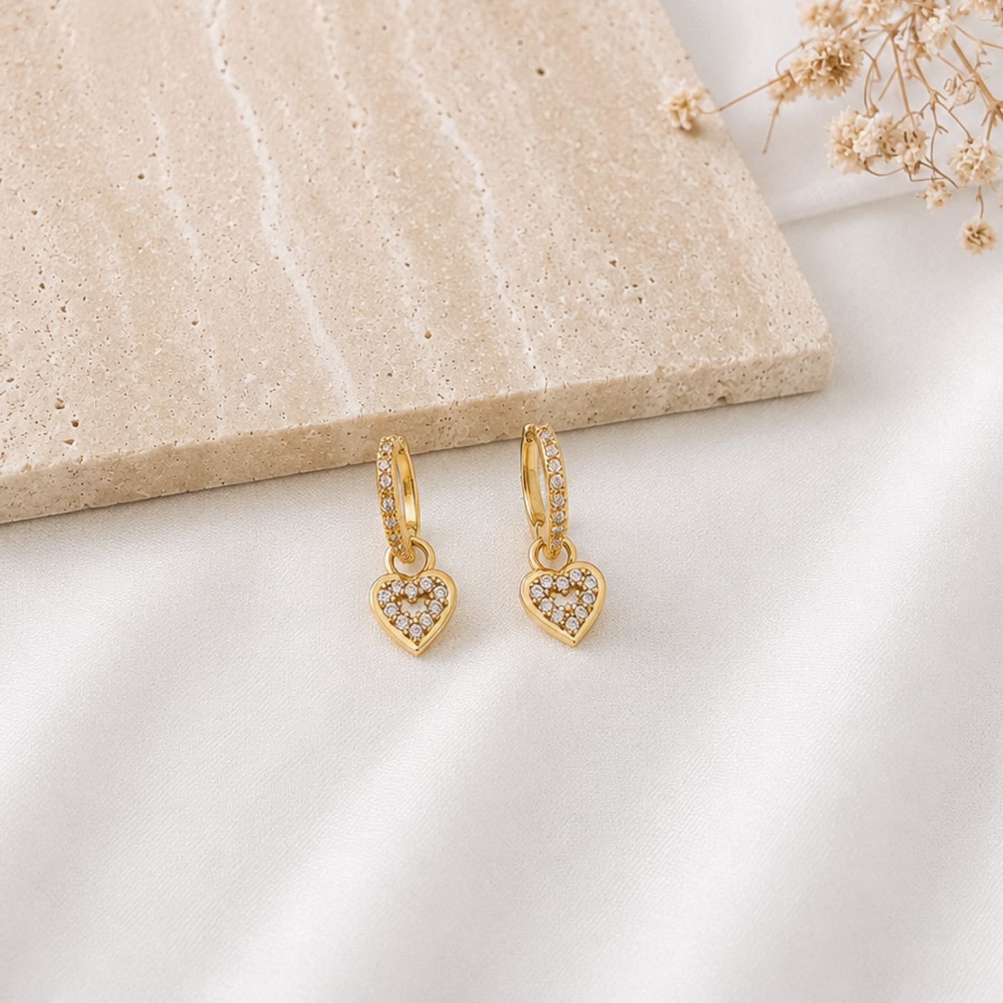Pair of gold-tone huggie hoop earrings with pavé cubic zirconia detailing and dangling heart charms fully adorned with sparkling clear stones. Elegant heart earrings with a timeless, romantic design, perfect for everyday wear, special occasions, or gifting.