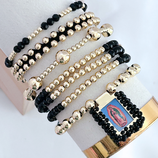 Three beaded bracelets with black and gold beads on a white surface.