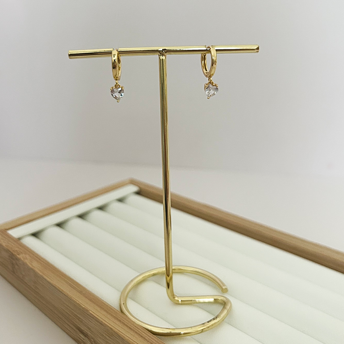 Gold huggie hoop earrings with dangling crystal heart charm on jewelry stand