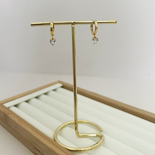 Gold huggie hoop earrings with dangling crystal heart charm on jewelry stand