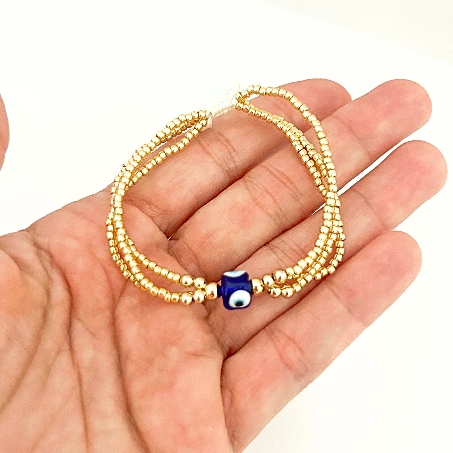 Handmade adjustable bracelet featuring shimmering gold beads and a traditional evil eye charm for a timeless look.