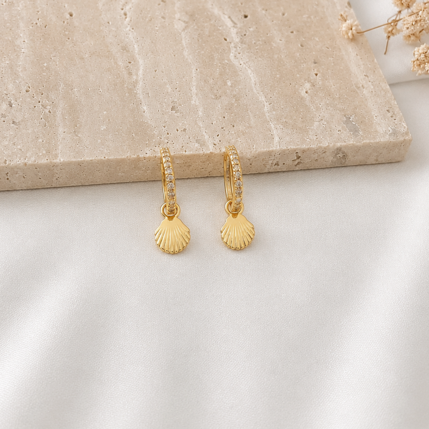 Pair of gold-tone huggie hoop earrings with sparkling pavé cubic zirconia detailing, each featuring a dangling seashell charm. Elegant beach-inspired earrings that add a subtle coastal touch to everyday and vacation looks.