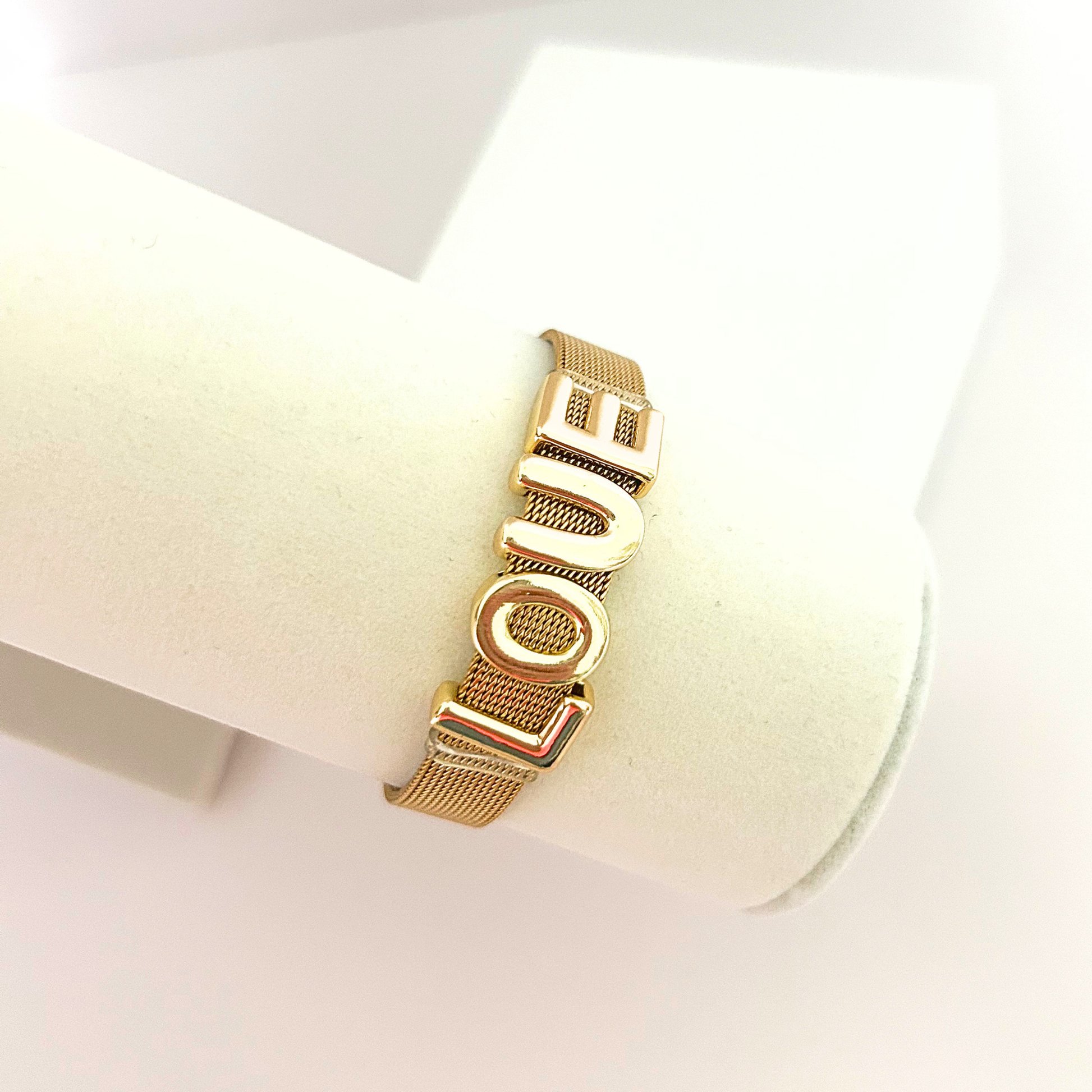 Elegant gold-tone mesh bracelet with LOVE centerpiece displayed on a jewelry stand.