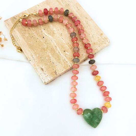 Handcrafted statement necklace featuring faceted pink gemstone beads with gold spacers and a carved green heart centerpiece. A colorful, elegant accessory designed to add a romantic touch to any outfit.