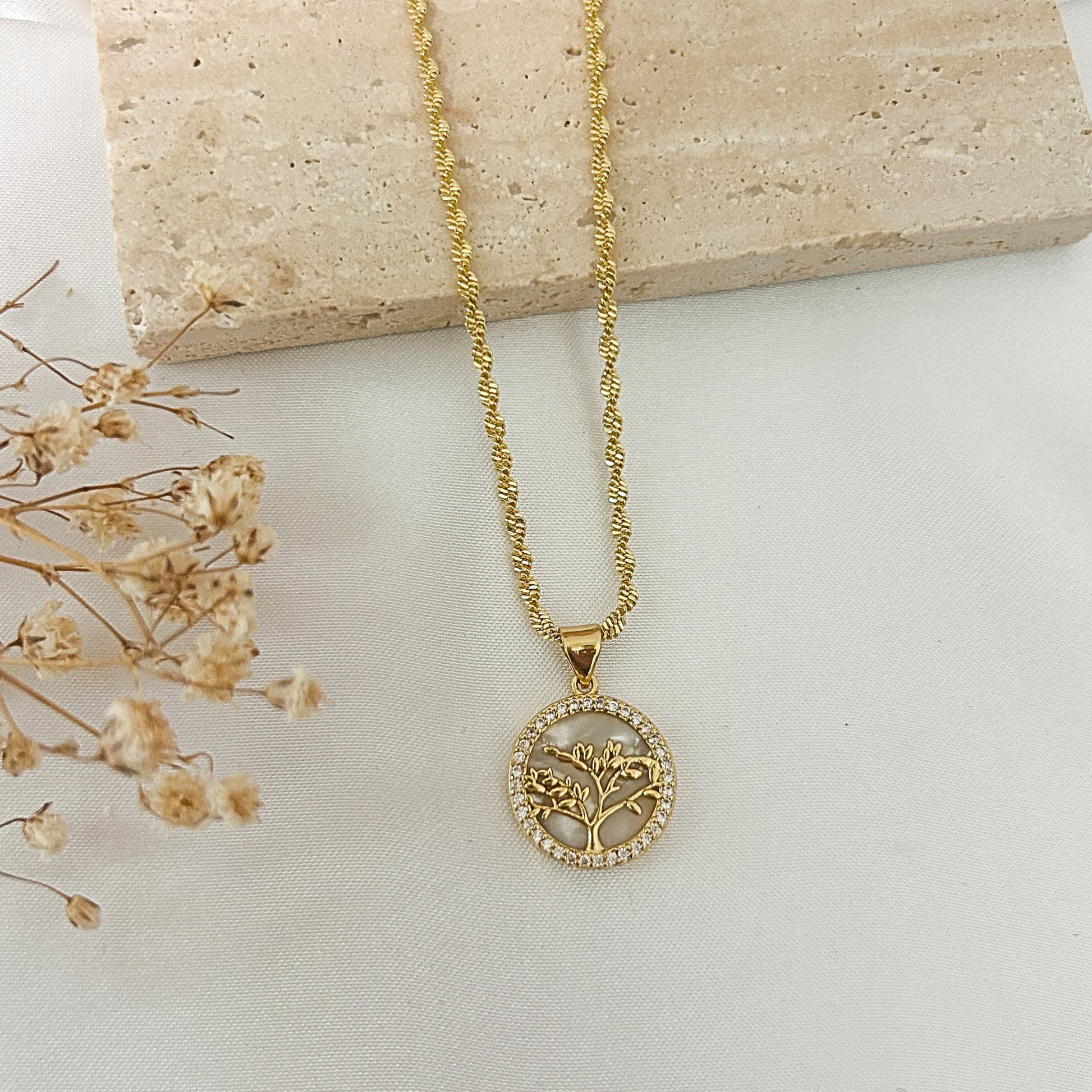 Gold Tree of Life pendant necklace featuring a mother-of-pearl background, sparkling cubic zirconia border, and textured gold chain, displayed on a neutral minimalist background.