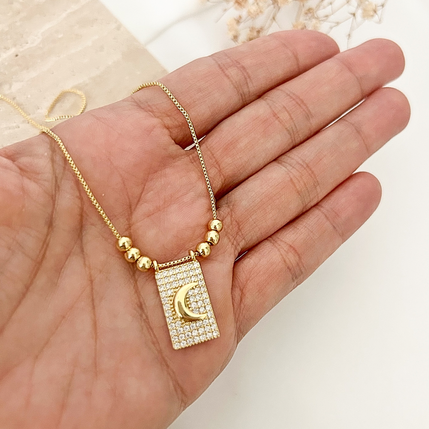 Close-up of a moon pendant necklace with crystal detailing and gold bead accents, shown in hand to highlight its size and intricate craftsmanship.