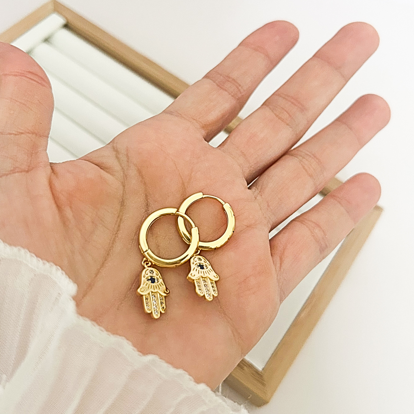 Pair of gold hoop earrings with Hamsa hand charm held in open palm