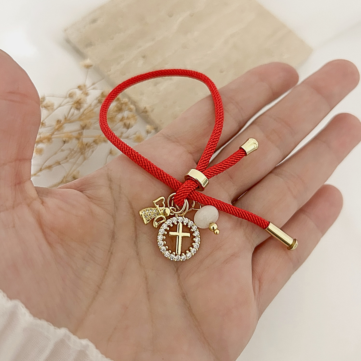 Hand holding red Saint cross charm bracelet to show size