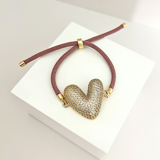 Adjustable mauve cord bracelet with a crystal-studded gold heart centerpiece, combining elegance and sparkle.