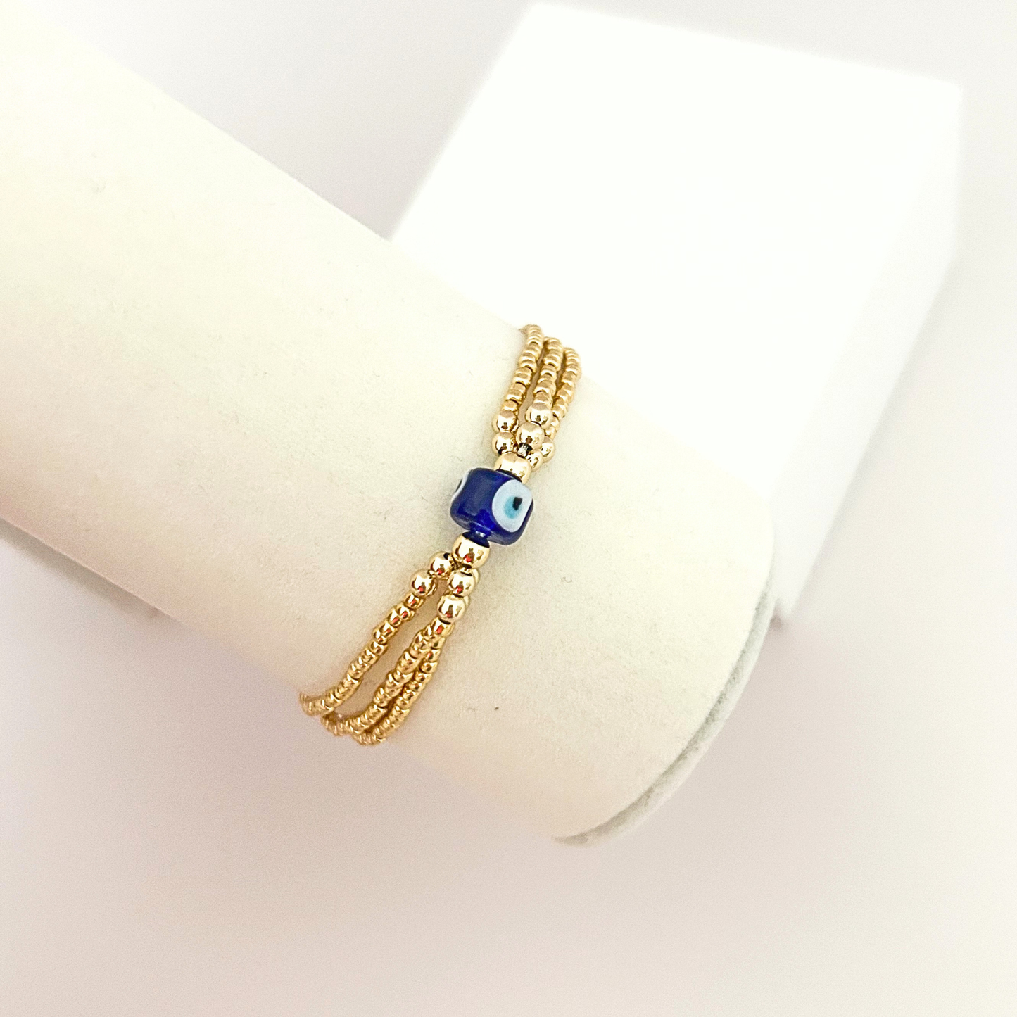 Adjustable gold-tone bracelet with three delicate strands and a handcrafted blue evil eye bead centerpiece.