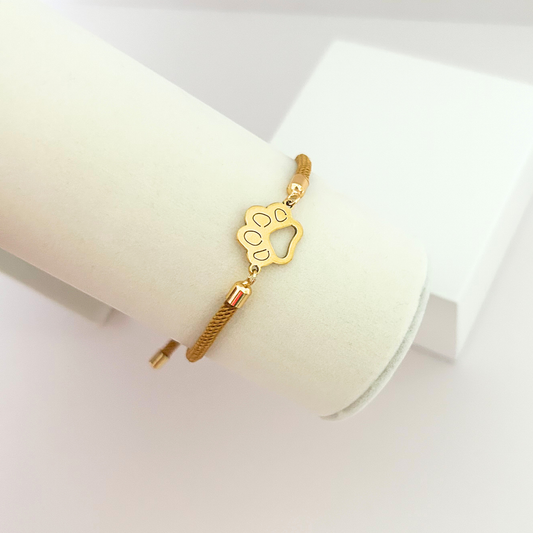 Minimalist pet paw bracelet with gold-tone charm and adjustable camel cord.