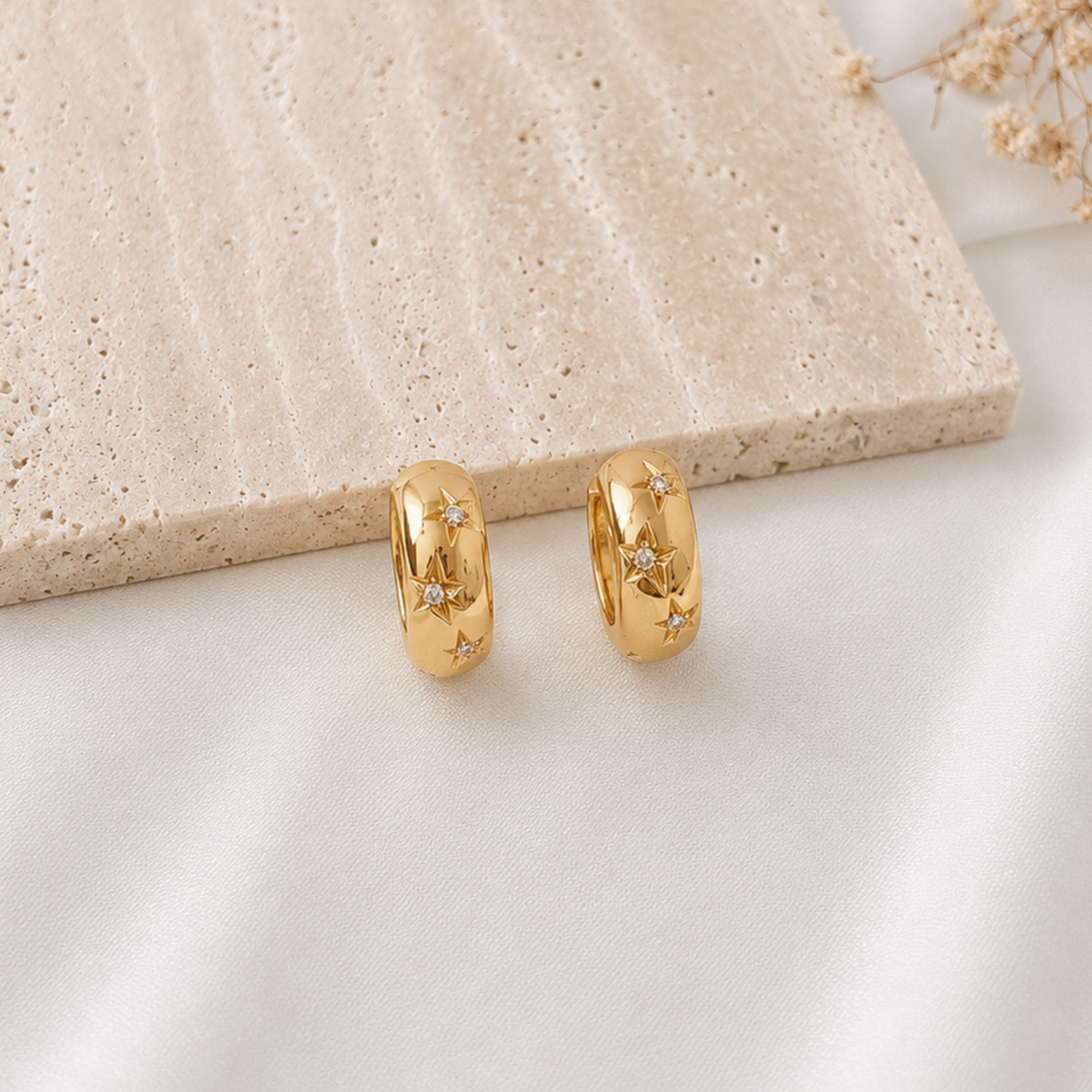 Pair of polished gold-tone huggie hoop earrings featuring engraved celestial star designs accented with sparkling cubic zirconia. Minimalist celestial earrings with a modern, elegant style, perfect for everyday wear or stacking with other gold jewelry.