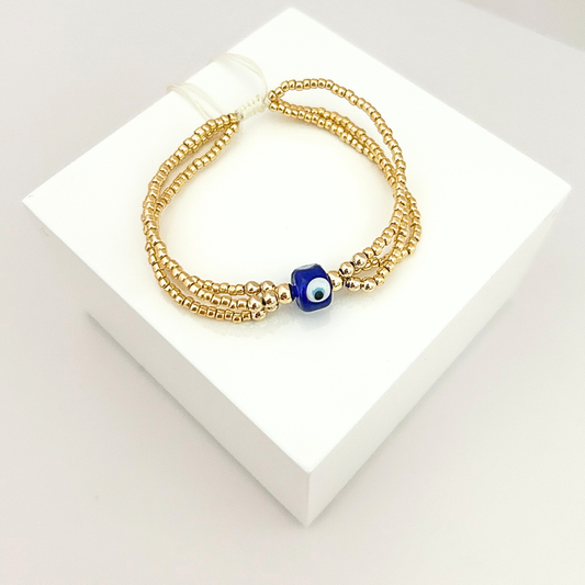Elegant triple-strand gold beaded bracelet featuring a blue evil eye charm, designed for protection and everyday style.