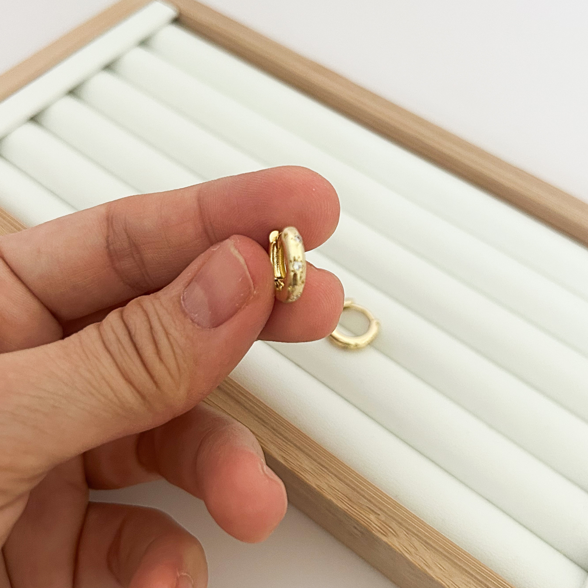 Small gold huggie hoop earring held between fingers — close-up detail