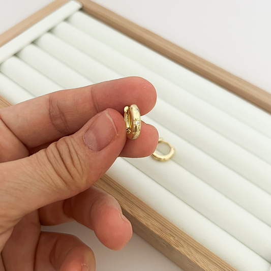 Small gold huggie hoop earring held between fingers — close-up detail