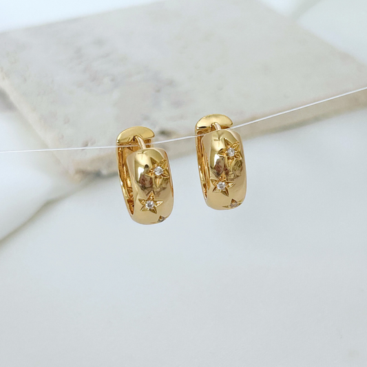 Gold hoop earrings with embedded stones on a marble surface