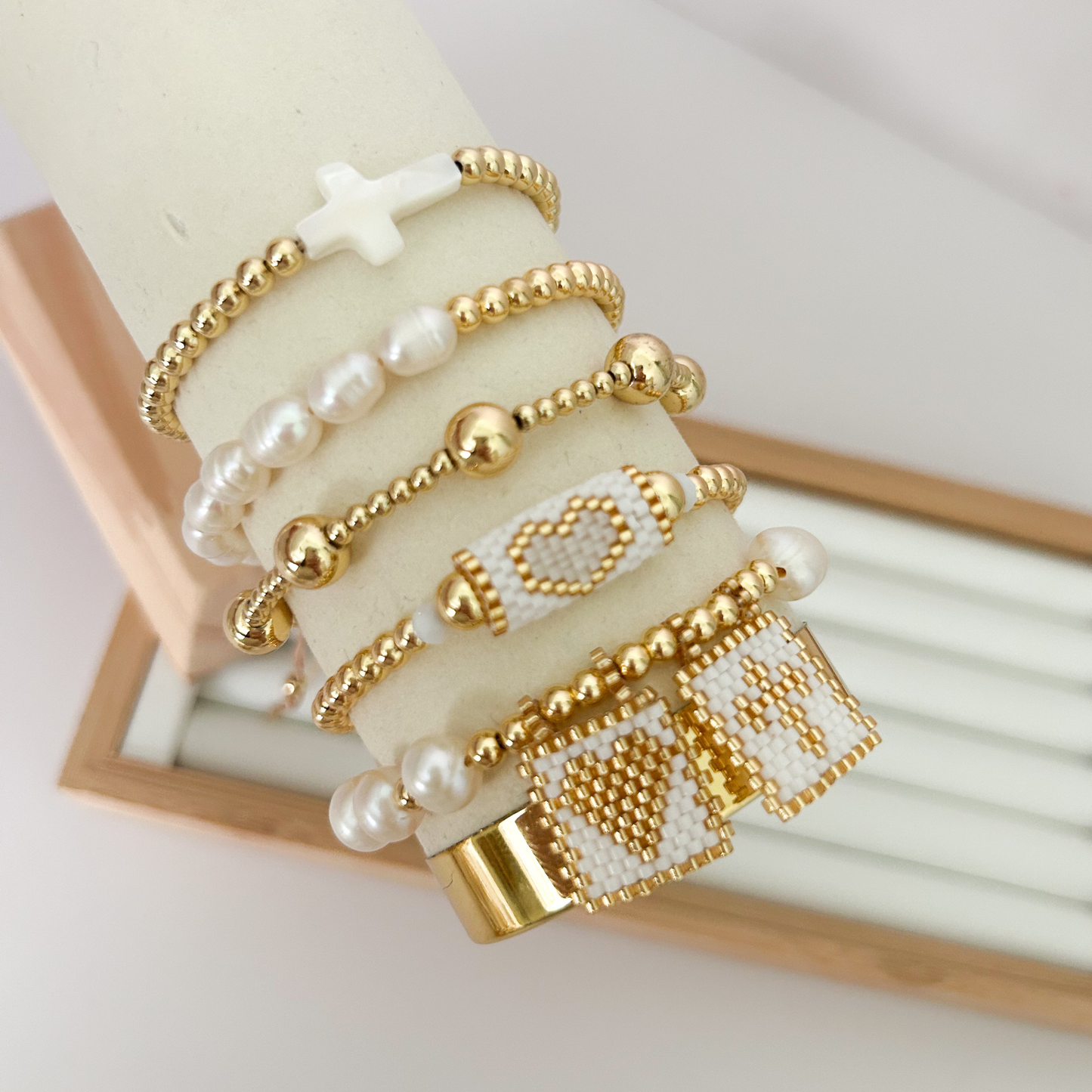 Handwoven miyuki pearl cross gold bracelet set on jewelry stand