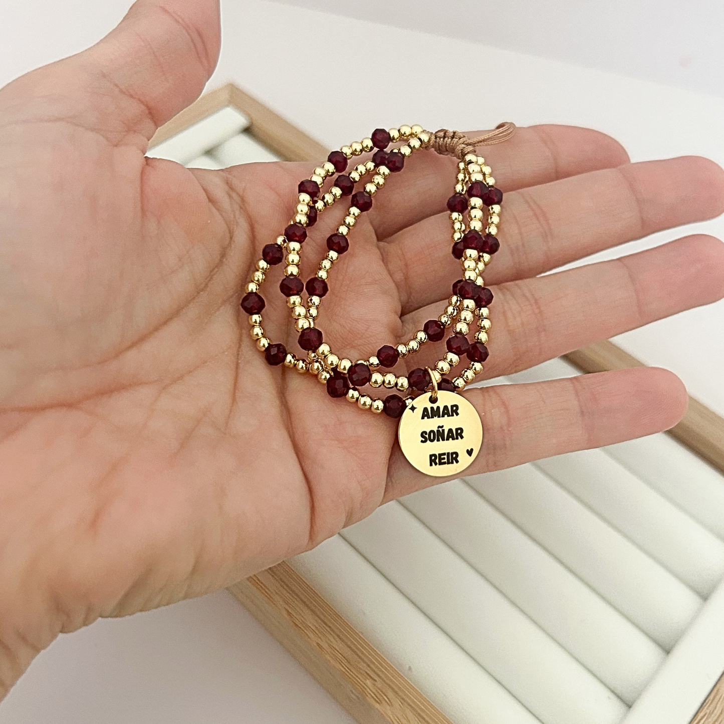 Hand holding burgundy and gold wrap bracelet with engraved motivational pendant.