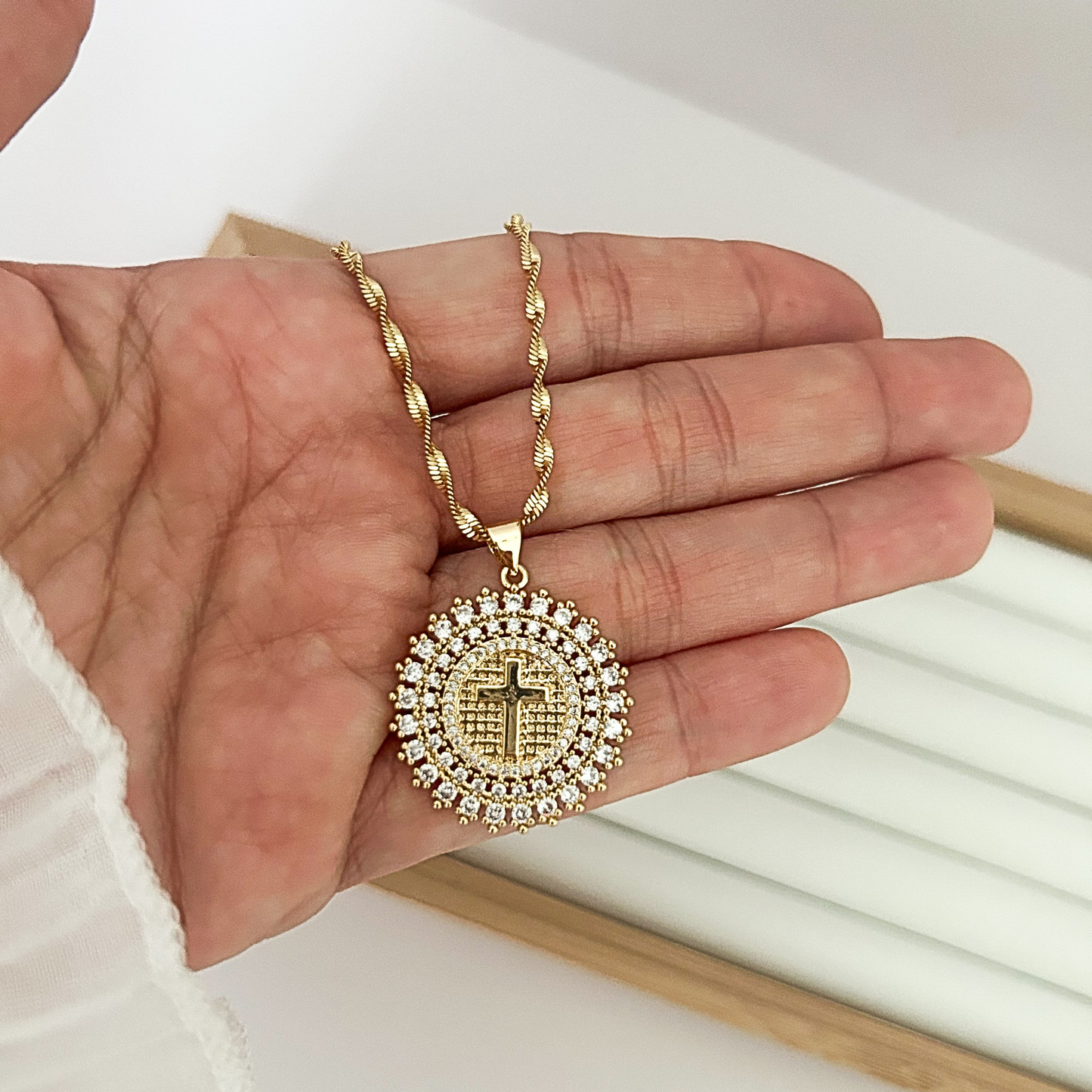 Women’s gold Christian necklace with detailed cross charm held in hand.