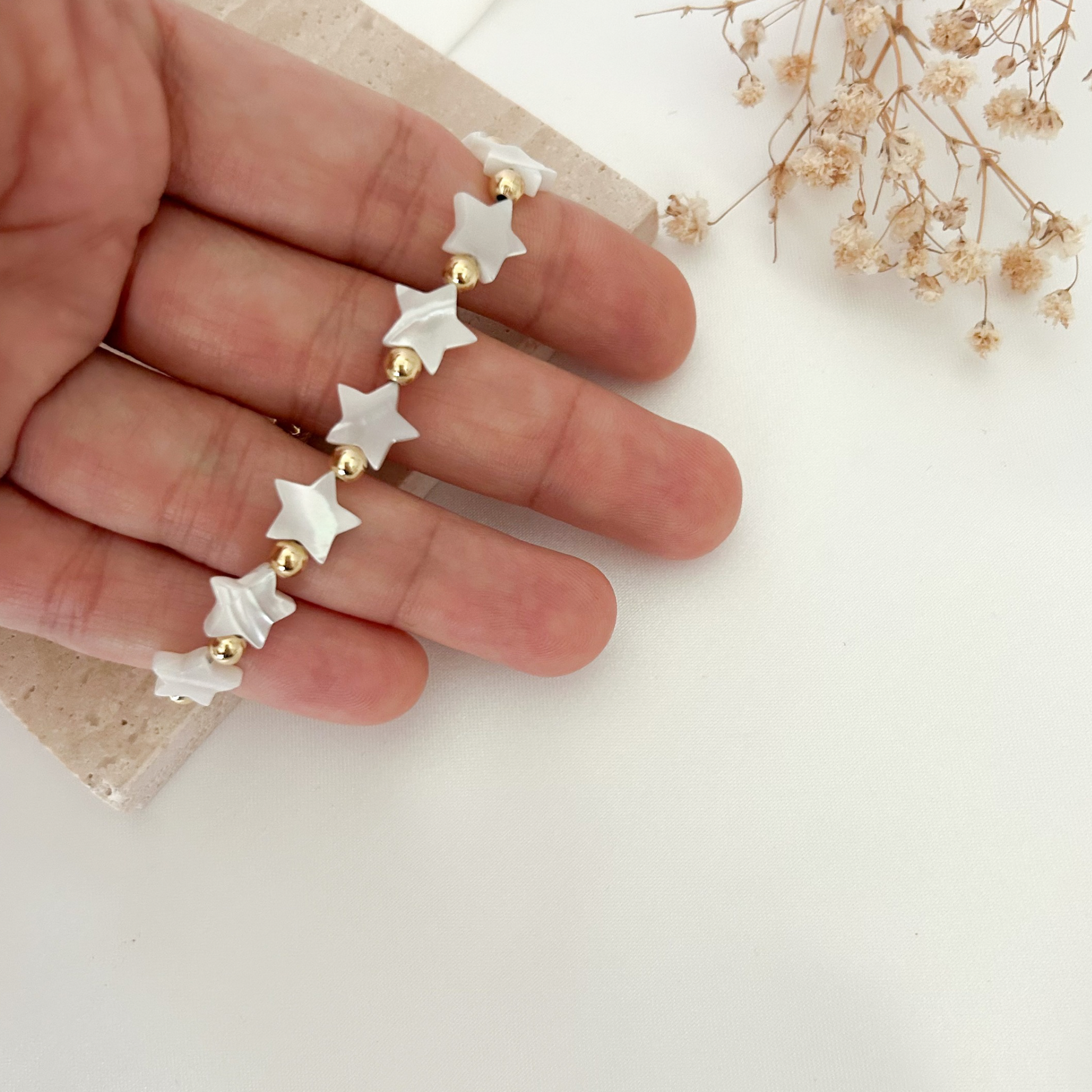 Adjustable bracelet featuring white star-shaped beads with gold-tone accents, styled on a hand against a soft neutral background with dried flowers.