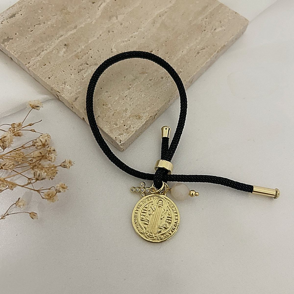 Black charm bracelet with gold Saint Benedict medal on a stone tray