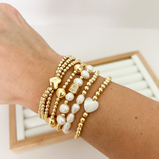 Gold beaded bracelet stack with baroque pearls and heart charm styled on wrist