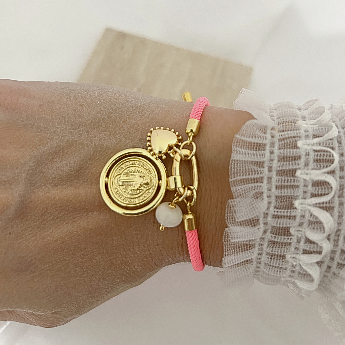 Neon pink adjustable bracelet with gold charms worn on the wrist