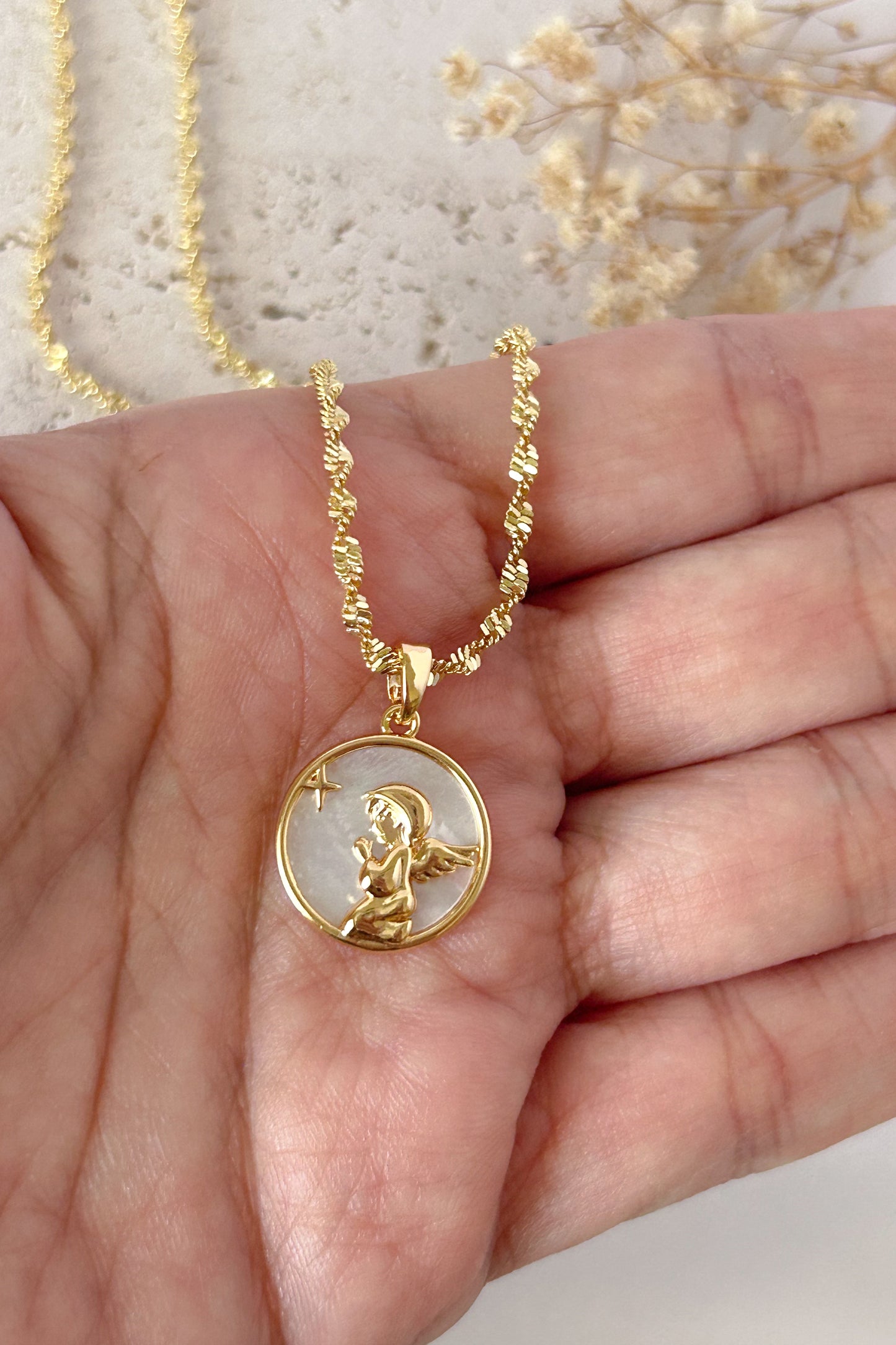 Gold necklace with a pendant held in a hand against a neutral background