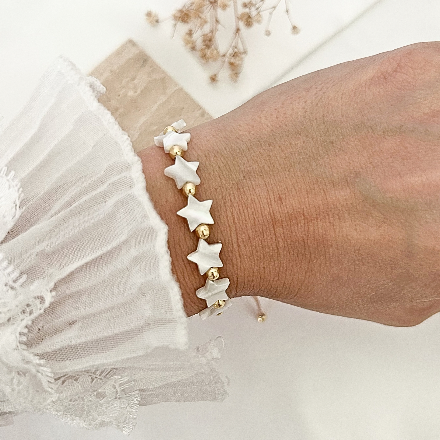 Delicate handmade bracelet with glossy white star beads, gold-tone spacer beads, and an adjustable cord closure, worn on the wrist with a lace sleeve.
