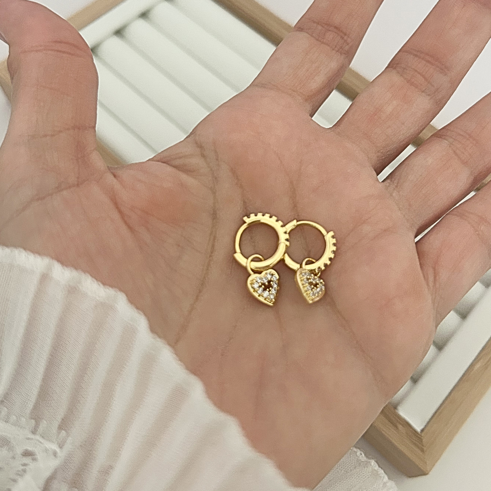 Gold huggie hoop earrings with white cubic zirconia pavé heart charm on jewelry stand