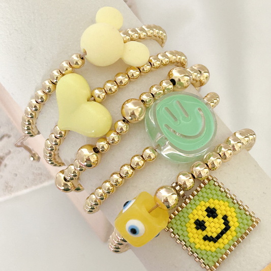 Gold bracelet with colorful beads and smiley face designs on a white background