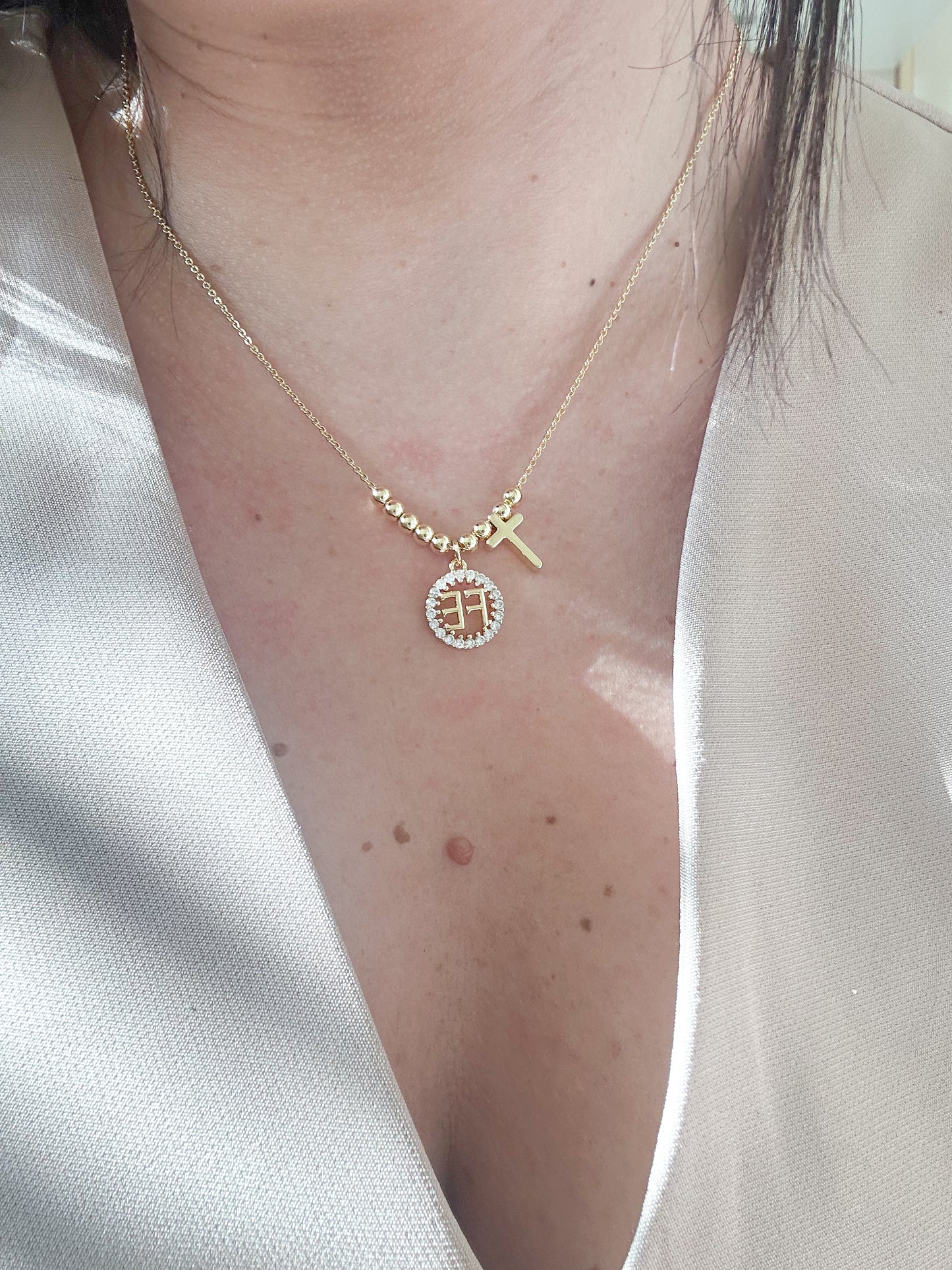 Gold necklace with a circular pendant on a person wearing a white shirt.