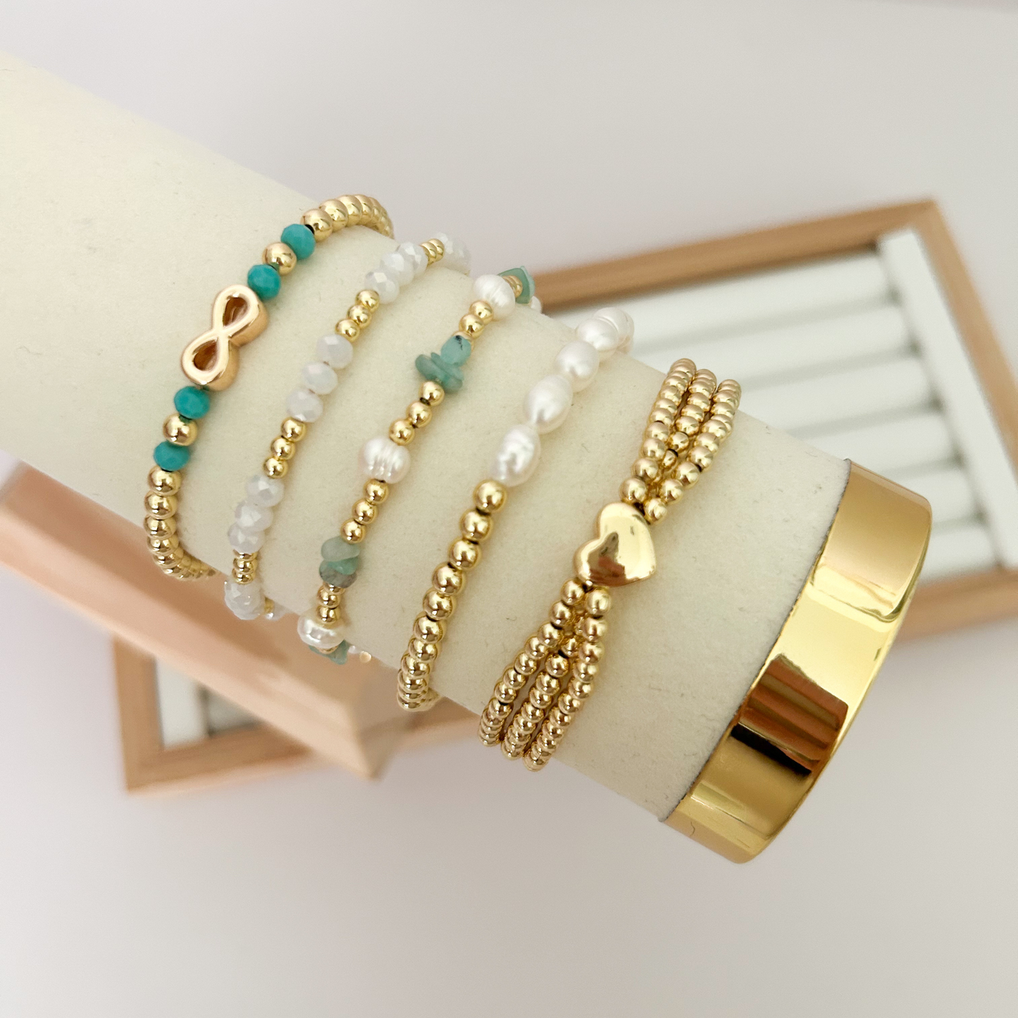 Gold bracelet set with turquoise and pearl accents displayed on jewelry stand