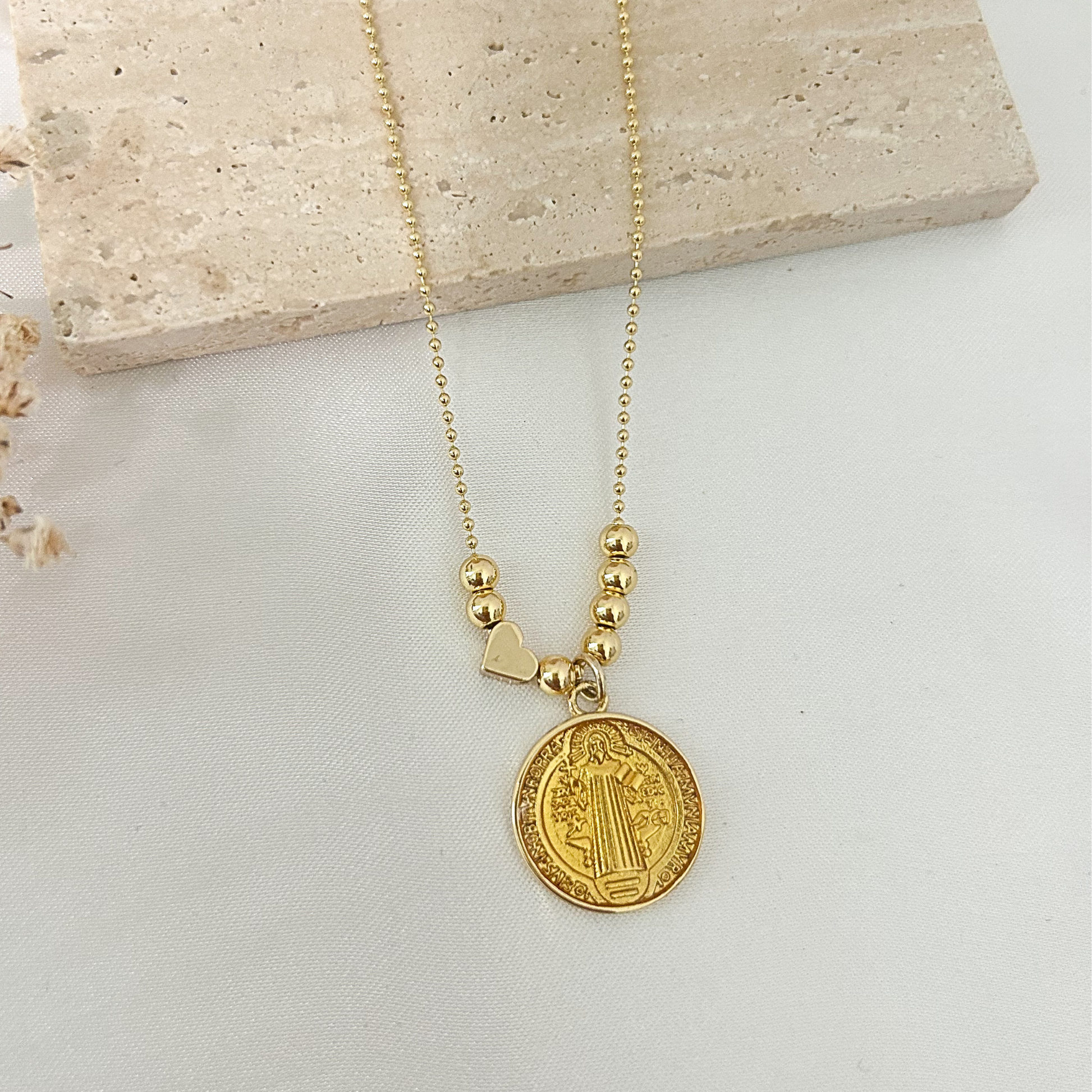Gold Saint Benedict medallion necklace with polished gold bead accents, shown in hand to highlight its size, elegant details, and delicate ball chain.