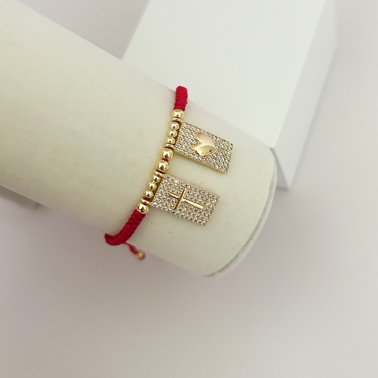 Side view of a red adjustable bracelet with gold-tone cross and heart charms embellished with shimmering crystals, showcased on a jewelry display.