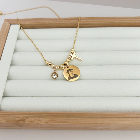 Gold necklace with a pendant featuring a portrait on a white jewelry display box.
