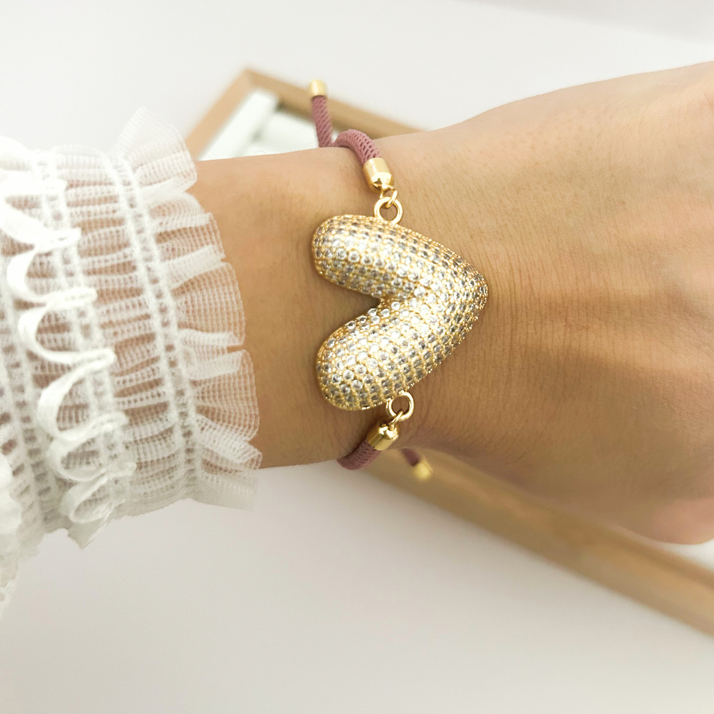 Gold heart charm bracelet with burgundy cord worn as everyday jewelry.