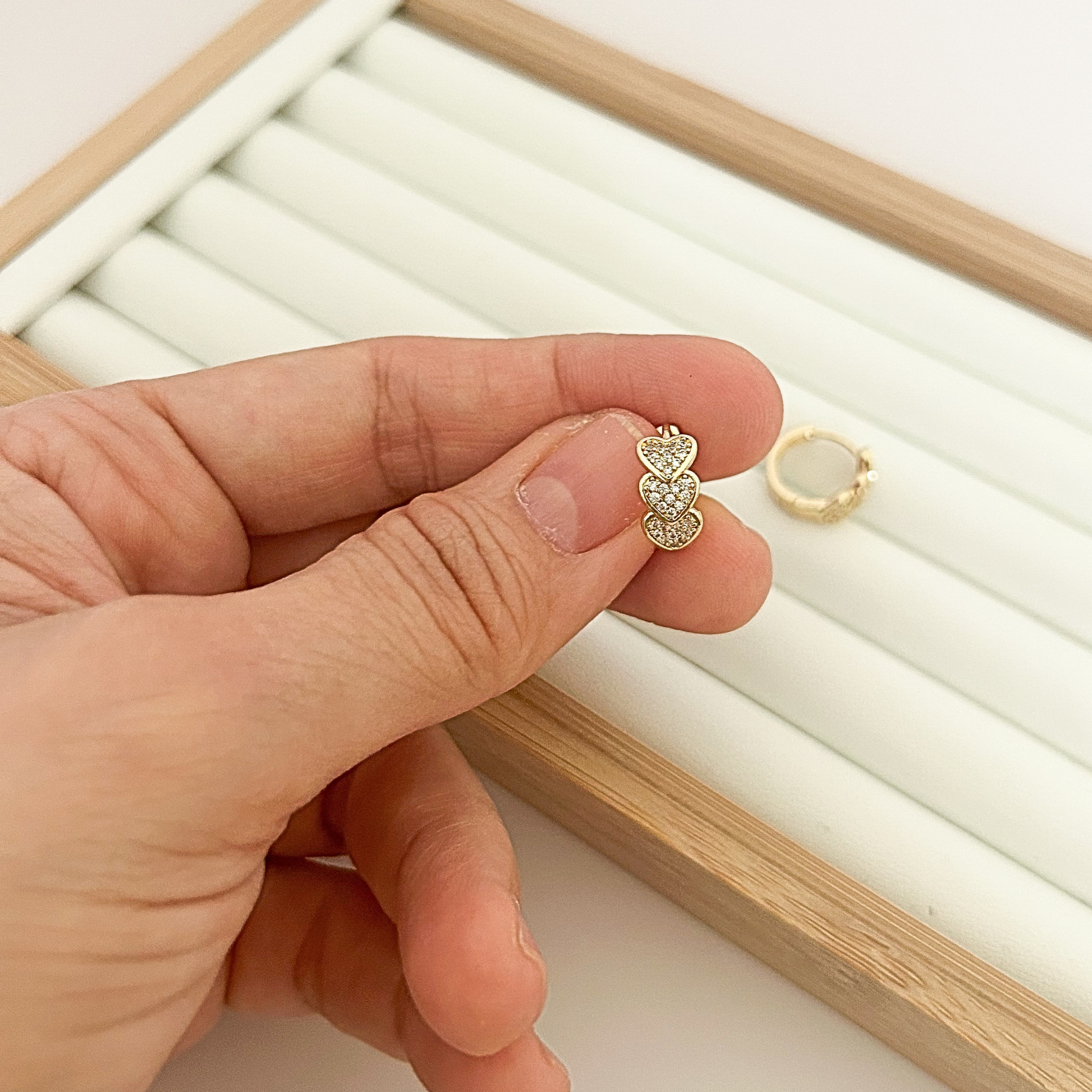 18K gold hoop earring with three stacked cubic zirconia hearts held in hand — close-up