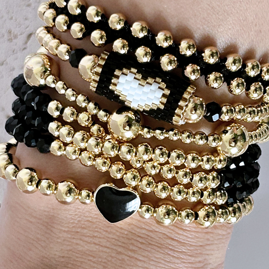 Gold and black beaded bracelets on a wrist against a neutral background
