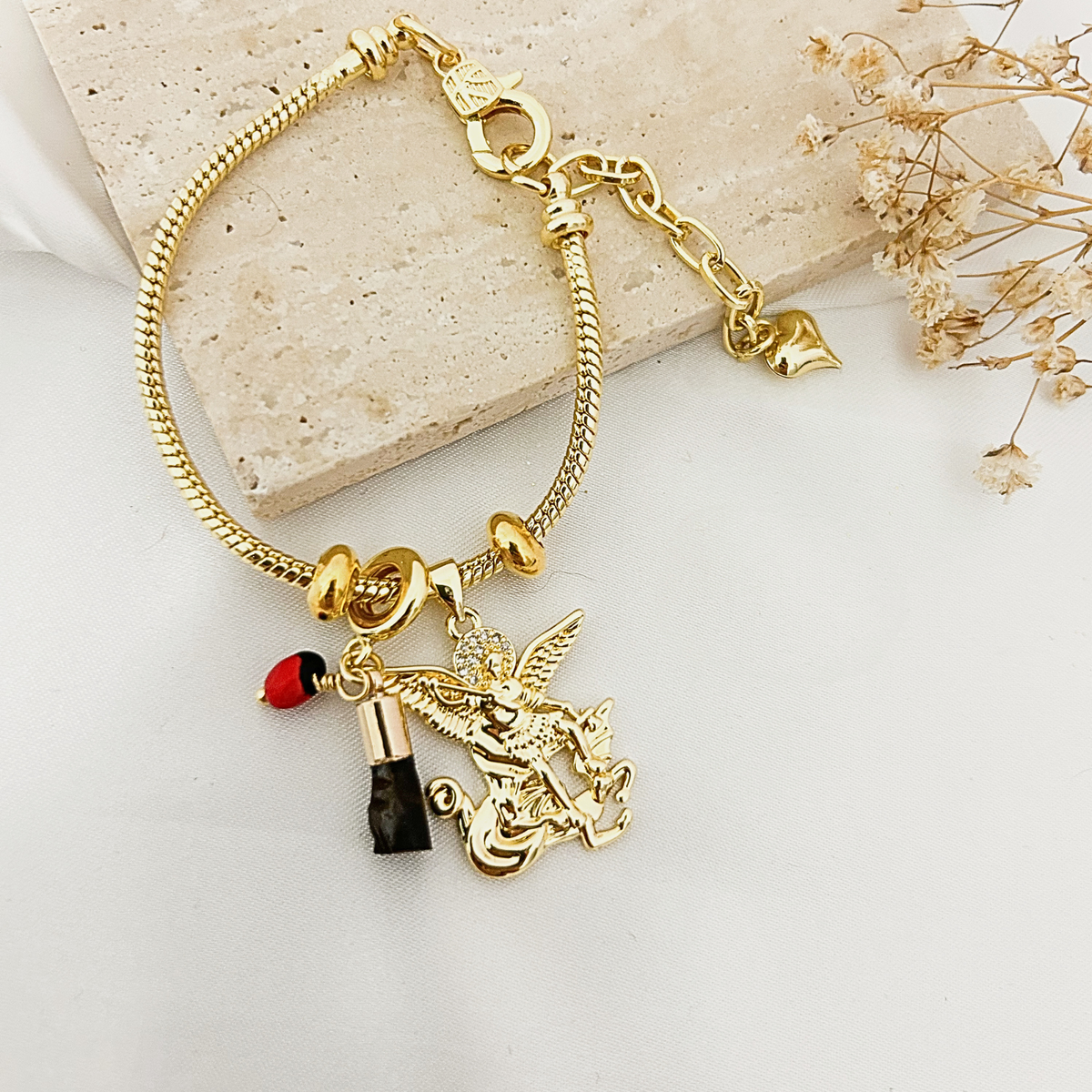 Gold Archangel Michael charm bracelet with azabache and peony charm on a stone tray