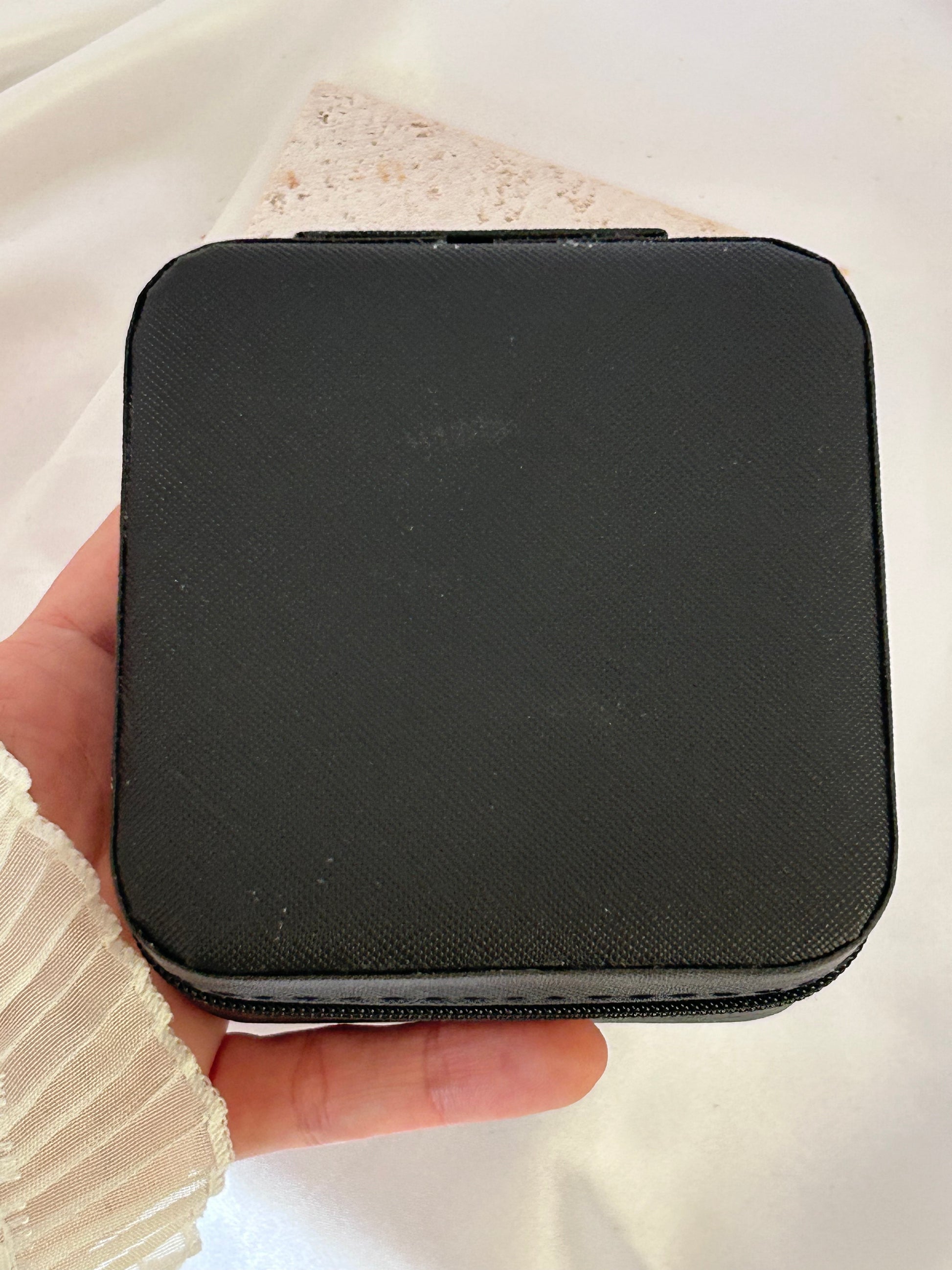 Black zippered pouch held in a hand against a light background